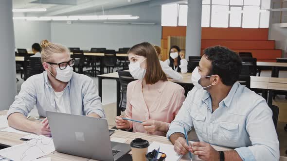 Multiethnic Diverse Colleagues in Protective Masks Working at Laptop Discussing Business Project