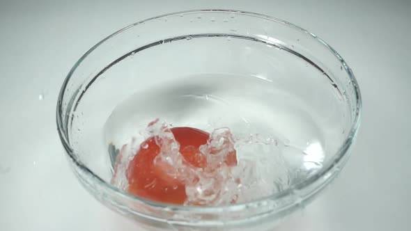 Slow Motion, One Red Tomato Falls Into the Water on a White Background. Ripe Tomato Is in a Glass