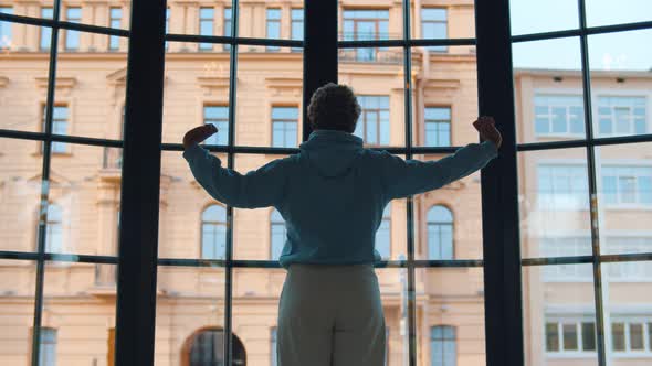 Back View of Young African Woman Stretching Looking Out of Large Panoramic Window