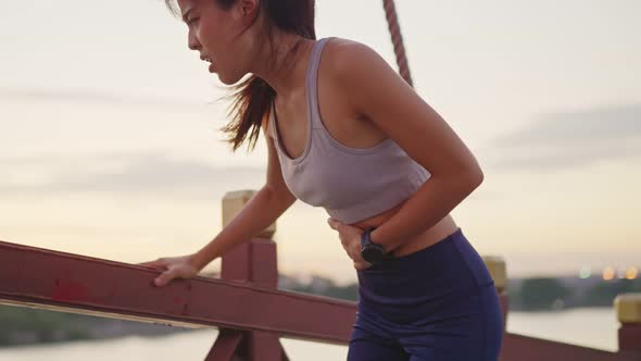 Asian young fit sport woman running and jogging in the park feeling sick with the pain on stomach