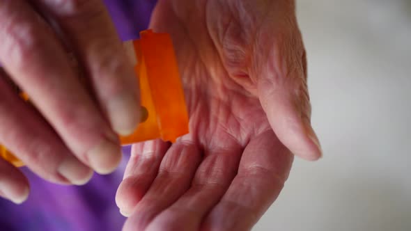 An elderly woman pouring pills from a prescription medicine bottle into her wrinkled, aged hand to c