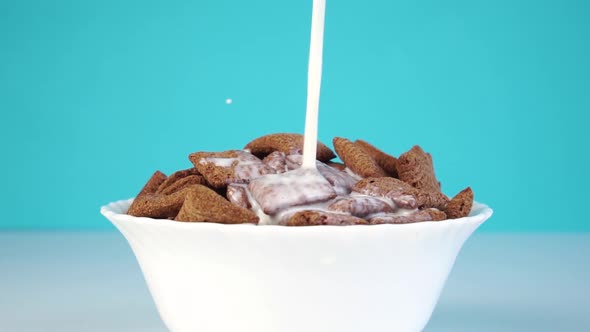 Milk is poured into a white bowl with chocolate cereal pads