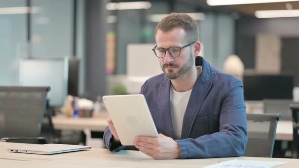 Middle Aged Businessman Celebrating Success on Tablet in Office