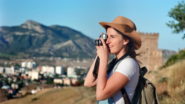 Smiling Young Travel Backpack Woman in Hat Taking Photo Using Camera Medium Shot