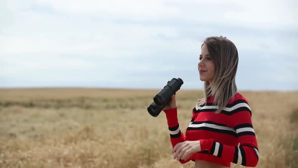 Woman in striped sweater looking in binocular in wheat field
