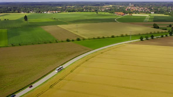 Flying over rural blooming fields following a driving bus passing by the peaceful summer landscape