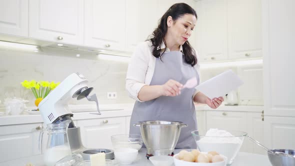 a Woman Cook with a Recipe Ingredients and a Mixer Prepares Pastries