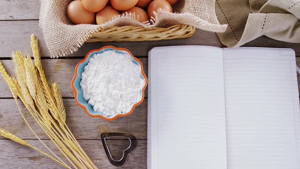 Book, eggs, flour, cookie cutter and wheat stem kept on a table