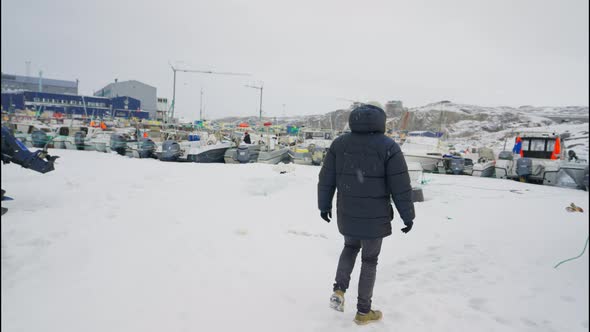 Man In Winter Coat Walking Towards Moored Boat In Snow Ilulissat