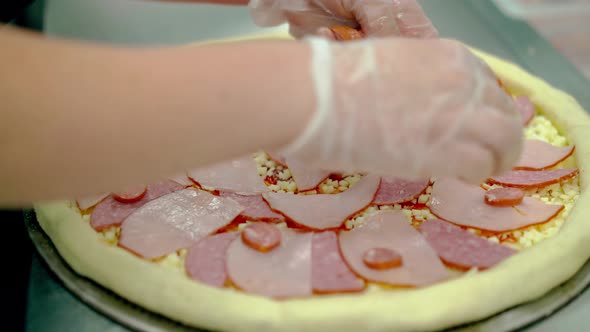 Cook Places Bacon and Smoked Sausage on Raw Pizza