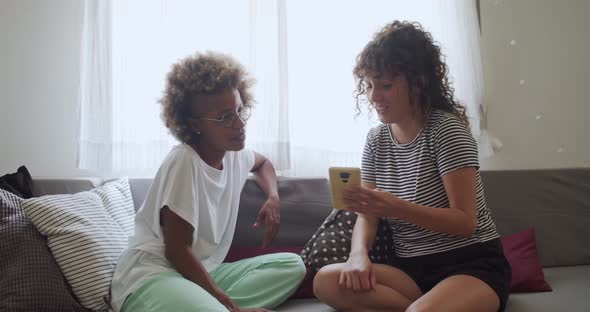 Two Multiethnic Female Friends Sitting Happily on the Sofa at Home