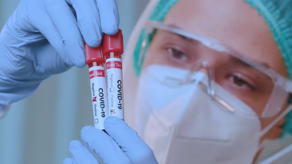 Doctor Wearing Protective Coverall Holds Test Tube with Blood Sample Covid-19