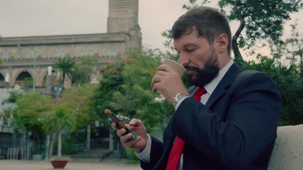 Businessman Bearded Man in an Expensive Suit Typing Something on His Phone While Sitting on a Park