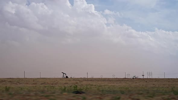 Pumpjack in field viewed from car driving by looking at dust storm