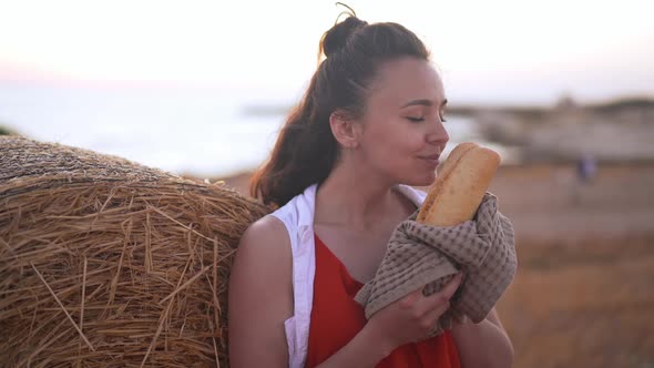 Slim Beautiful Young Woman Smelling Freshly Baked Bread Loaf Standing at Yellow Haystack on Rural