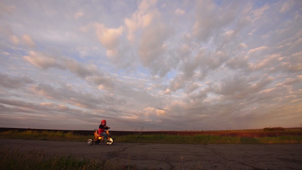 Children ride bicycles and dog one after another on a scenic rural road at sunset