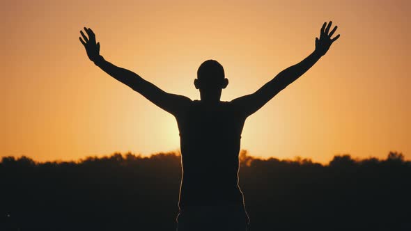 Silhouette of Man Against Sunset Raising Hands To Sides and Up. Slow Motion