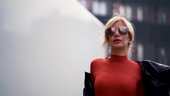 Portrait of a Blonde in a Red Dress, Dark Glasses and Bright Lipstick on Her Lips. She Walks Down a