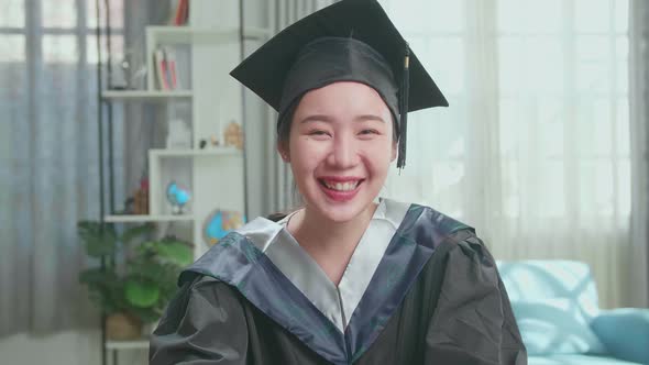 Asian Woman Wearing A Graduation Gown And Cap Having Video Call In Living Room