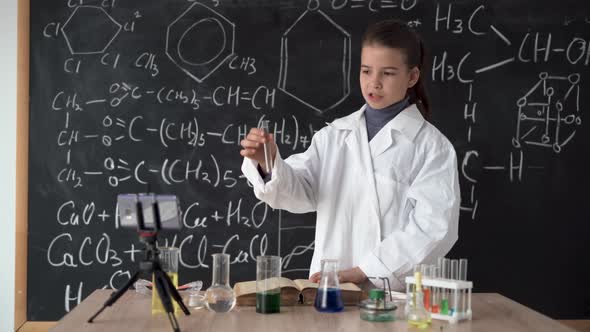 Little Scientist Girl in White Coat Leads an Online Video Blog Records Video Using Smartphone alt