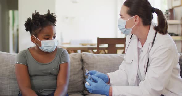 African american girl and caucasian female doctor wearing face masks, vaccinating