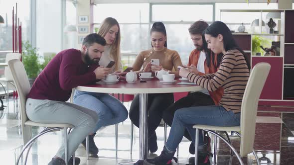 Group of Caucasian Friends Using Smartphones As Sitting Together in Cafe. Digital Addicted Man