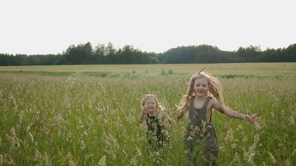 Two Girls in Dresses Run Across the Field at Sunset