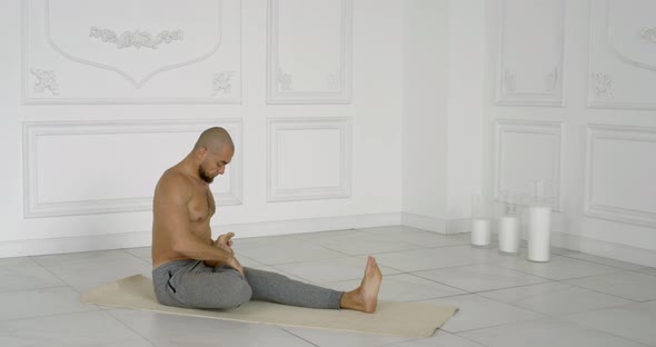 Flexible and Plastic Male Yogi with a Beard Doing Yoga on a Rug in a Bright Studio