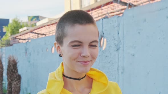  Portrait of Young Smiling Woman with Shaved Hair in Urban Background. 