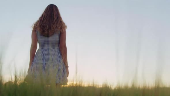 Woman In Striped Dress Walking Through Field At Sunset