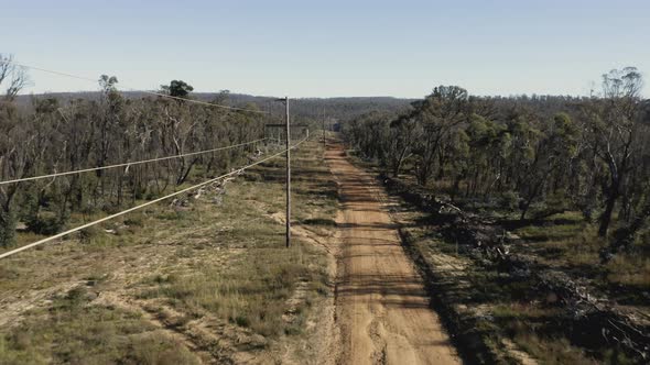 Drone aerial footage of telephone lines along a dirt road in regional Australia