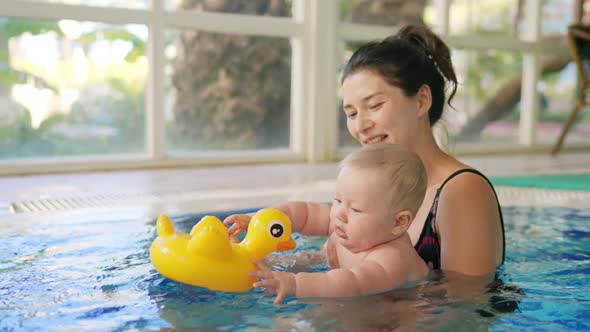 Happy Mother in Red Swimming Suit with Baby Son Surfing Water with Fun in Swimming Pool