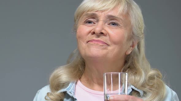 Senior Woman Tasting White Vitamin Pill and Drinking Water From Glass, Treatment