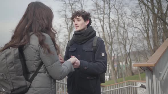 Portrait of Young Loving Caucasian Boy Holding Hands of Brunette Girl and Talking, Happy Guy with