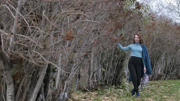 Young Redhaired Woman in a Blue Coat and Walks Against the Backdrop of the Old City