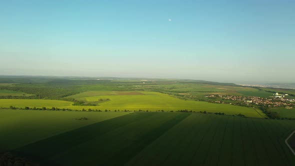 Aerial Descent Over Green Fields with Clear Blue Sky, Moon, Road and Small Town in the Background
