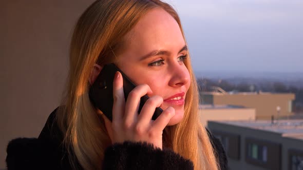 A Young Beautiful Woman Stands on a Balcony and Talks on a Smartphone - Face Closeup