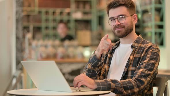 Cheerful Young Man Pointing with Finger in Cafe 