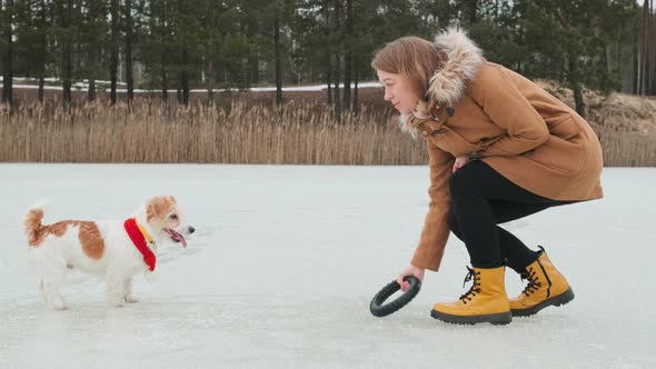 A girl in a coat and yellow boots plays in the winter on the ice of the lake with a dog