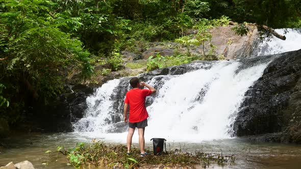 Traveler Man Enjoying Tropical Waterfall on Travel Vacation and Drinking Water