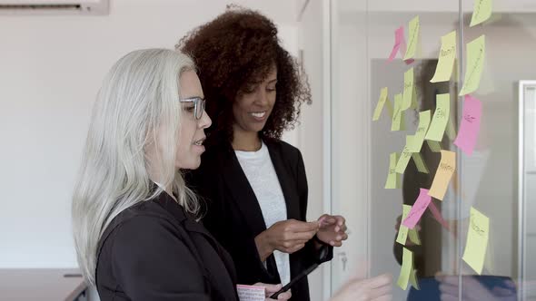 Happy Female Colleagues Sticking Memos on Glass Board