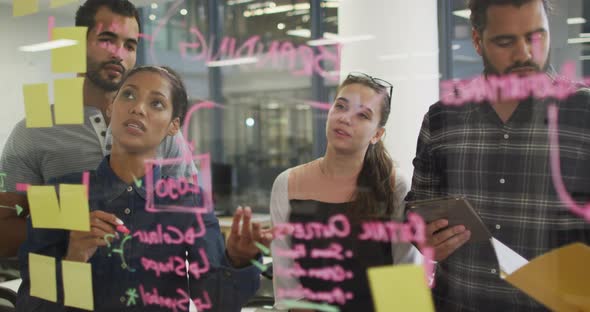 Diverse group of work colleagues brainstorming writing notes on glass wall