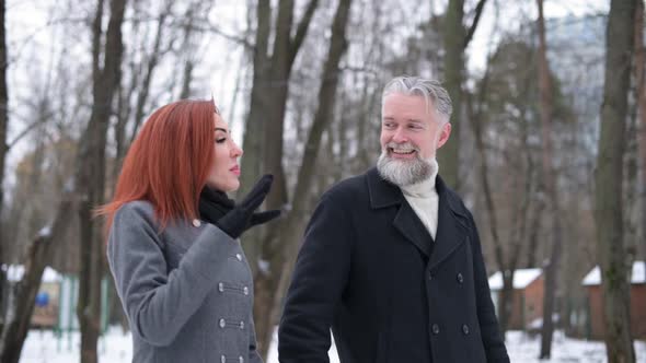 A close-up of a gray-haired man walking and chatting with a young woman