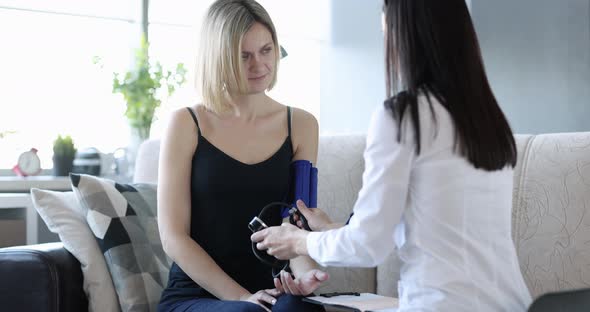 Medical Assistant Measures Blood Pressure of Young Female Patient at Home