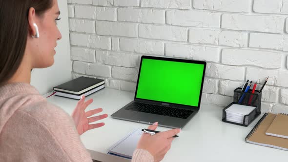 Woman teacher with pen in hand communicates talk speak with green screen laptop
