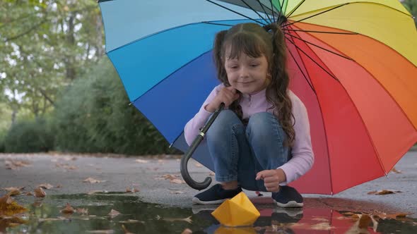 A Child with an Umbrella Plays in a Puddle.