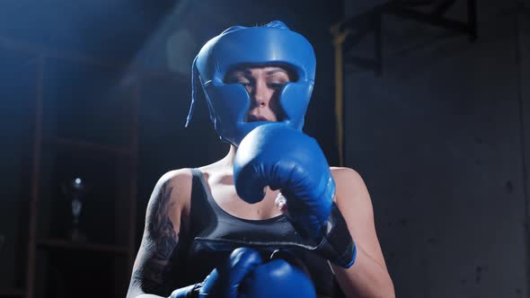 Tattooed Woman in Protective Soft Helmet Puts on Boxer Gloves