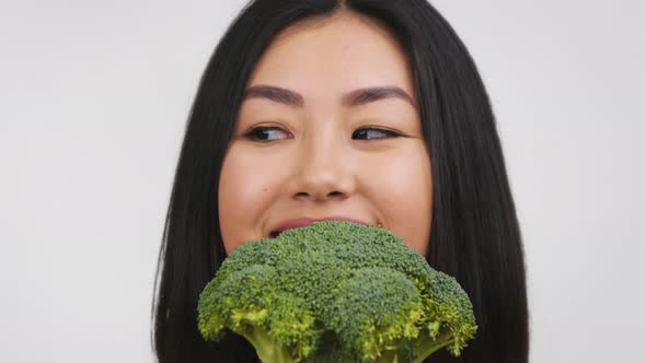 Happy Asian Woman Holding Broccoli Near Face Over White Background