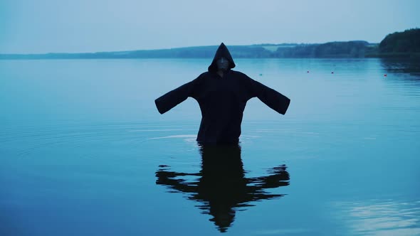 Terrible figure in a black robe in the water outdoor. Divination by Halloween