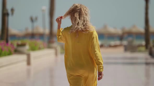 a Curly Blonde in a Yellow Fluttering Dress Goes to the Beach with Umbrellas on a Sunny Day